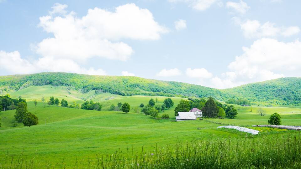 A green valley with rolling hills, a white barn, and a clear blue sky.