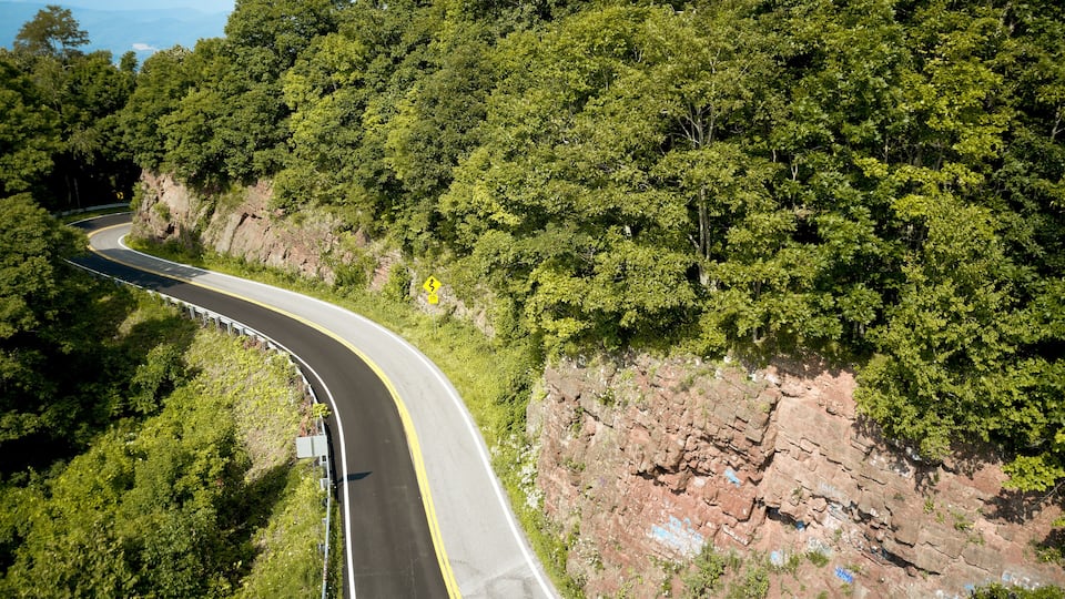 A winding mountain road surrounded by dense green forest and rocky cliffs.
