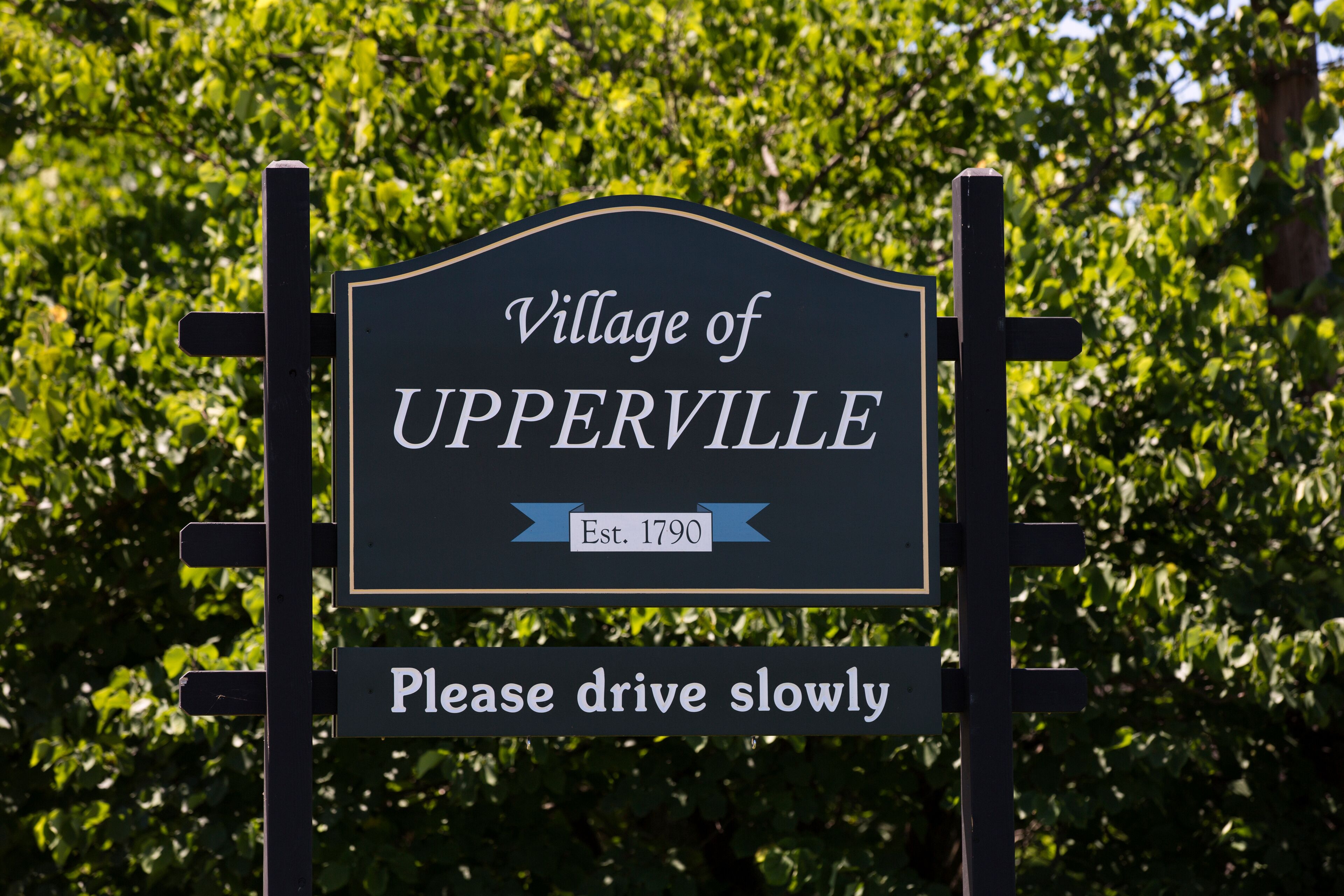 A sign for the Village of UPPERVILLE with a 'Please drive slowly' message.