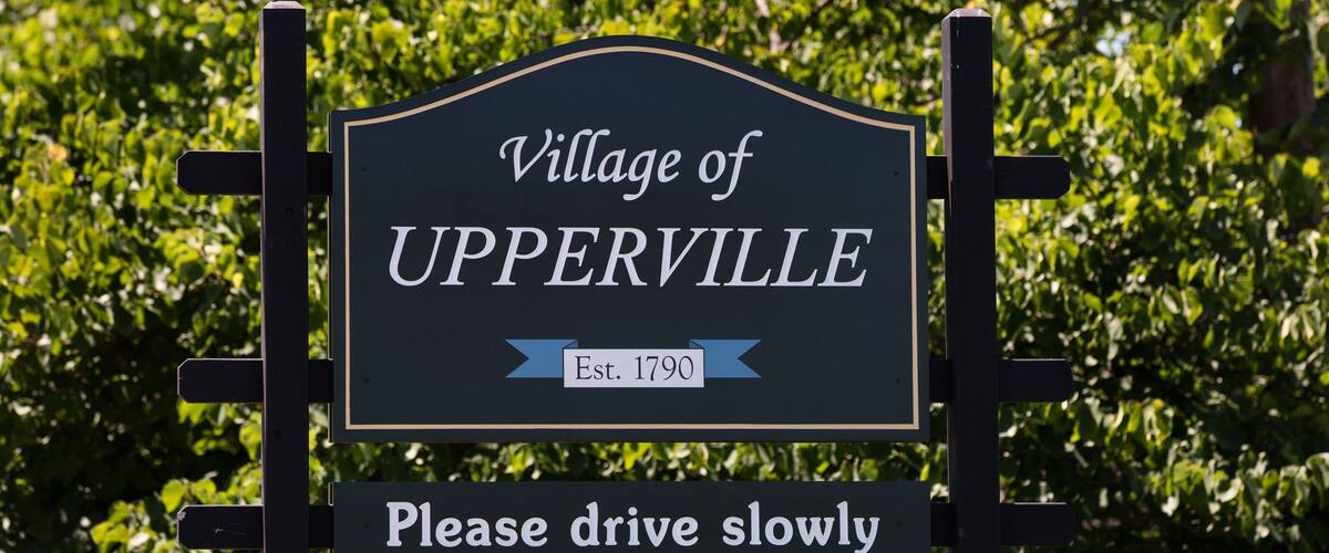 A sign for the Village of UPPERVILLE with a 'Please drive slowly' message.