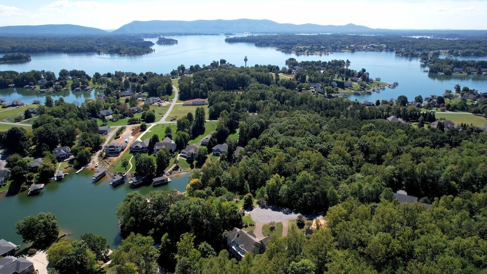 A lakeside community with houses, a lighthouse, and surrounding greenery.