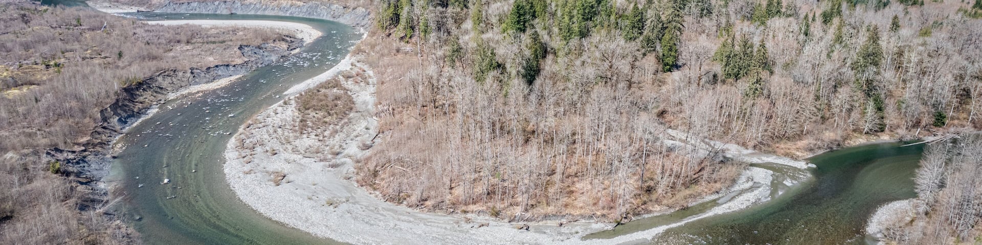 A winding river through a forested valley with mountains in the background.