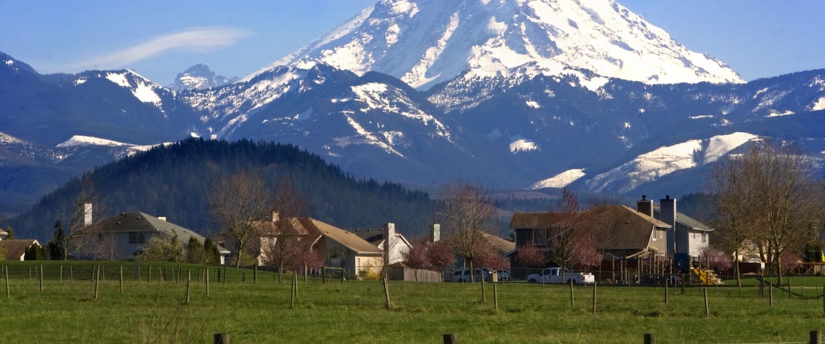 A snow-capped mountain, houses, and a green field.