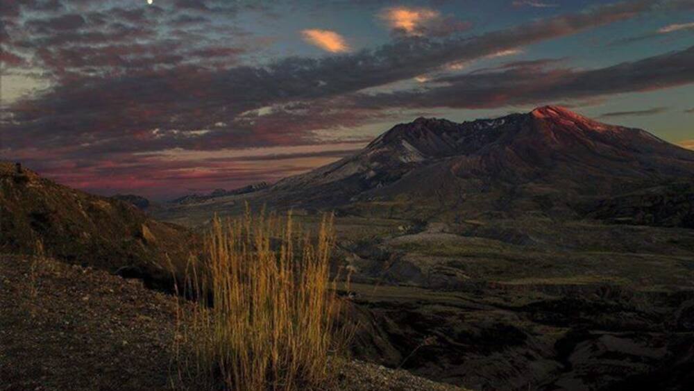 Une montagne dont le sommet est teinté d’une couleur rougeâtre, entourée d’une vallée où la végétation est clairsemée.