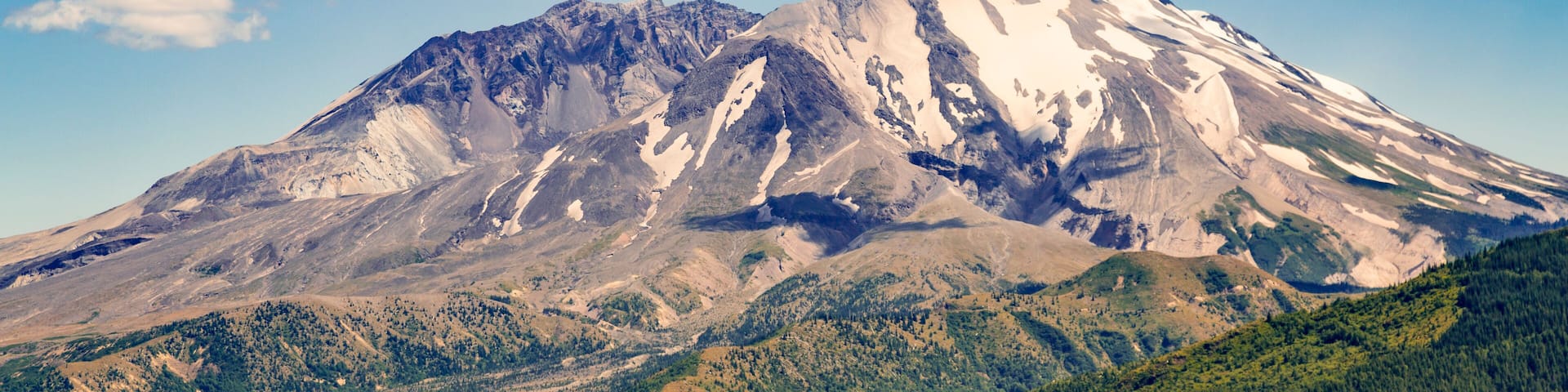 A snow-capped mountain with a clear sky and forested valleys.