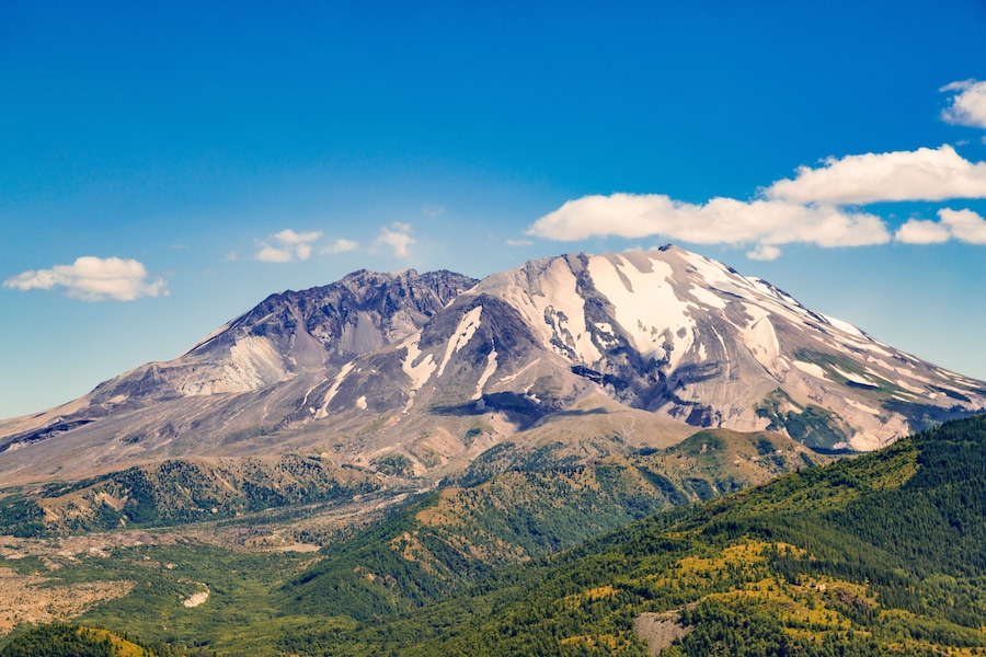A snow-capped mountain with a clear sky and forested valleys.