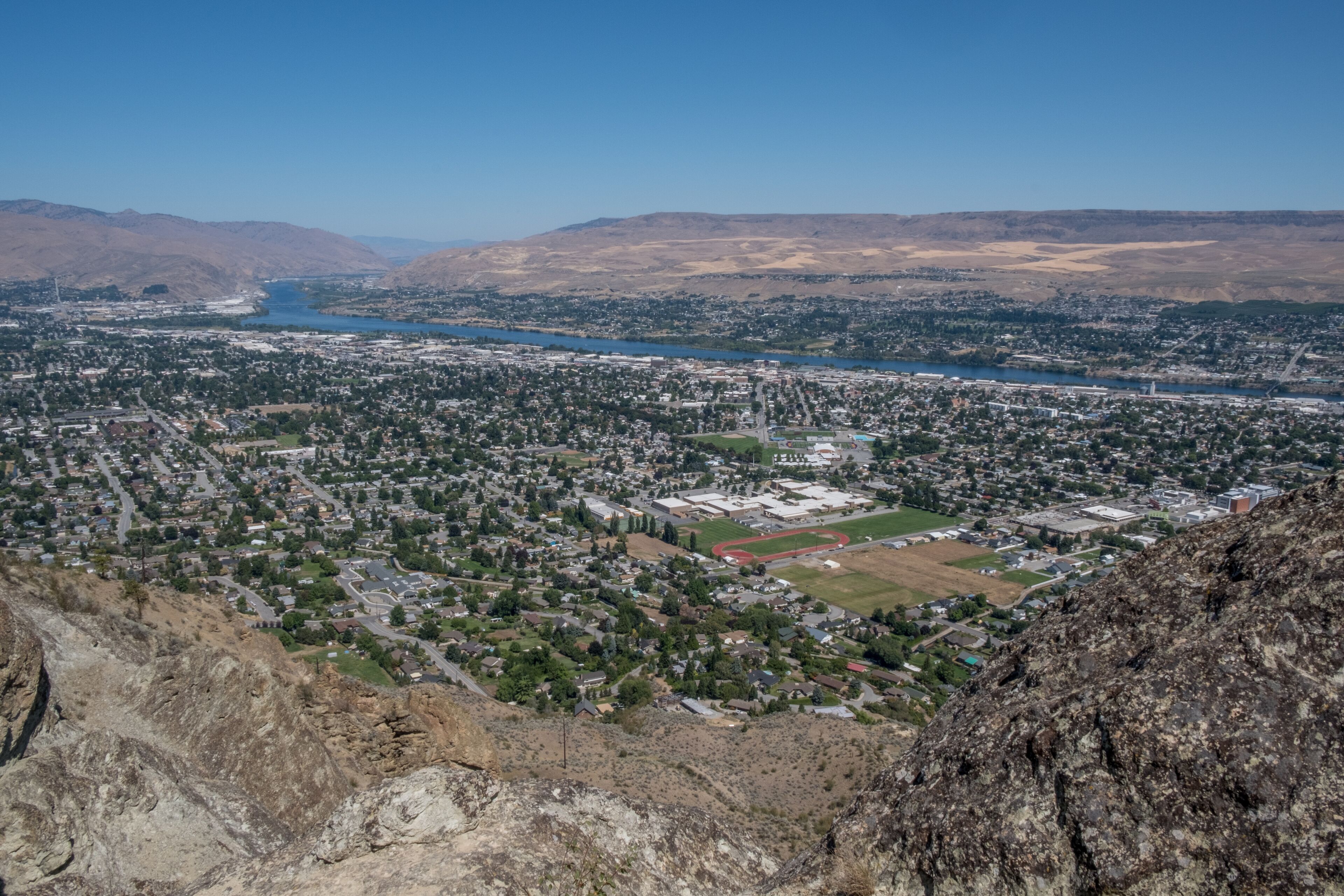 A cityscape with a river, mountains, and a school building.