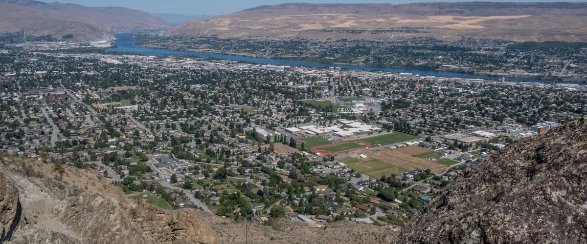 A cityscape with a river, mountains, and a school building.