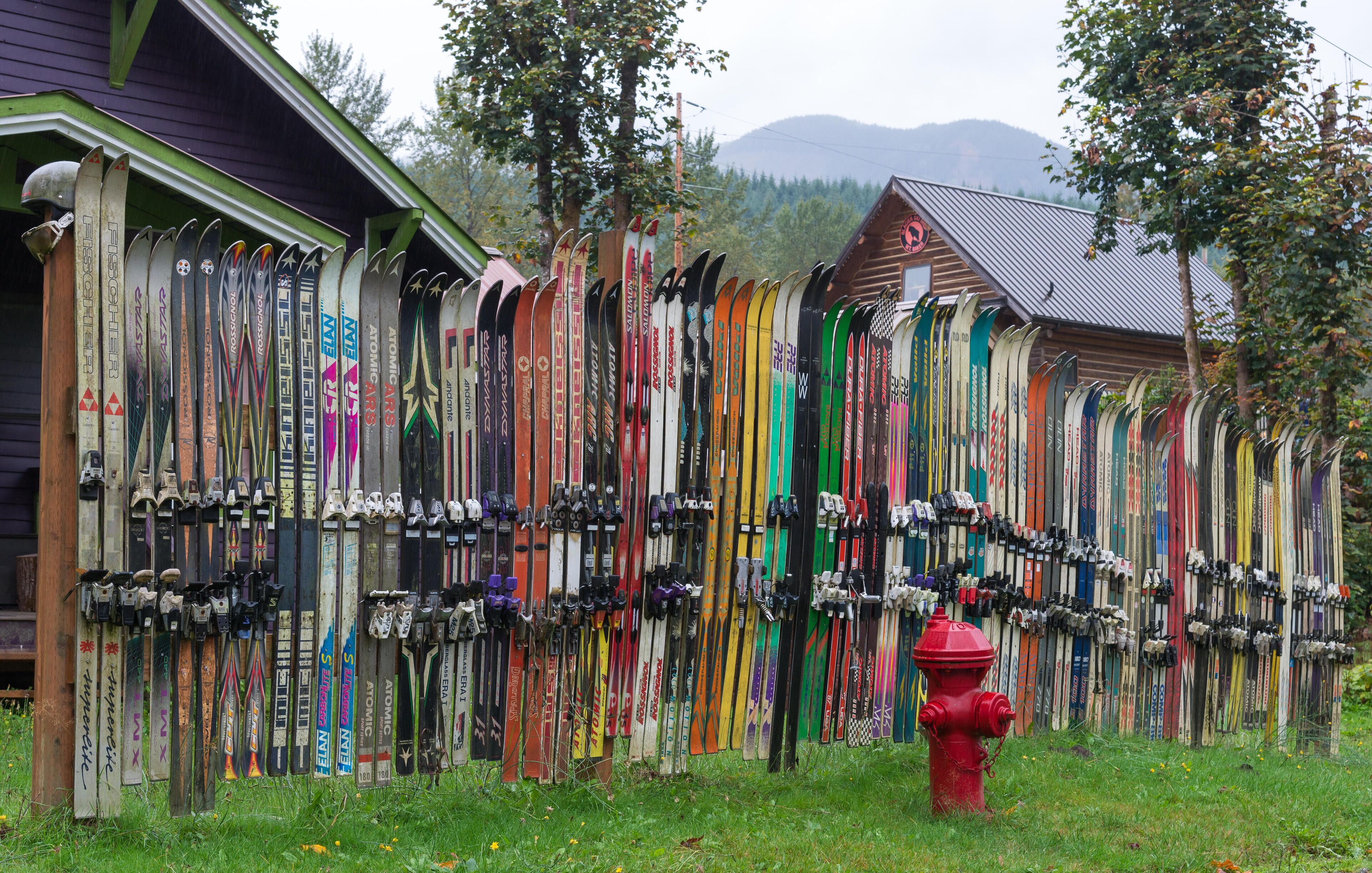 A row of skis leaning against a building with a red fire hydrant in the foreground.