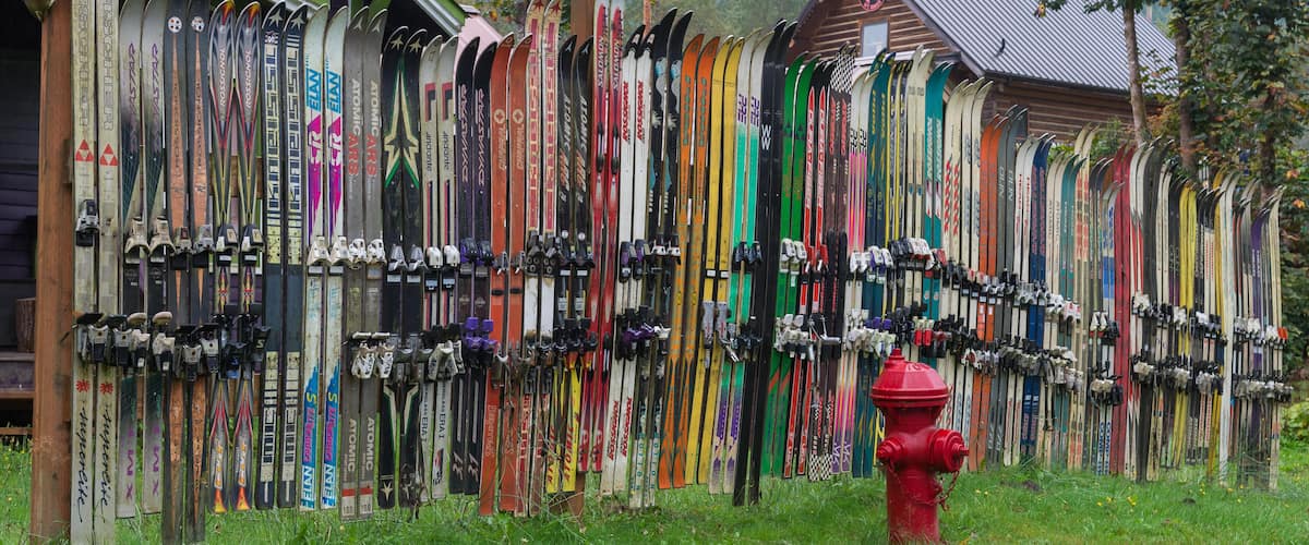 A row of skis leaning against a building with a red fire hydrant in the foreground.