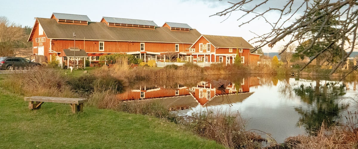 A red building with a white fence, a pond, and a picnic table.