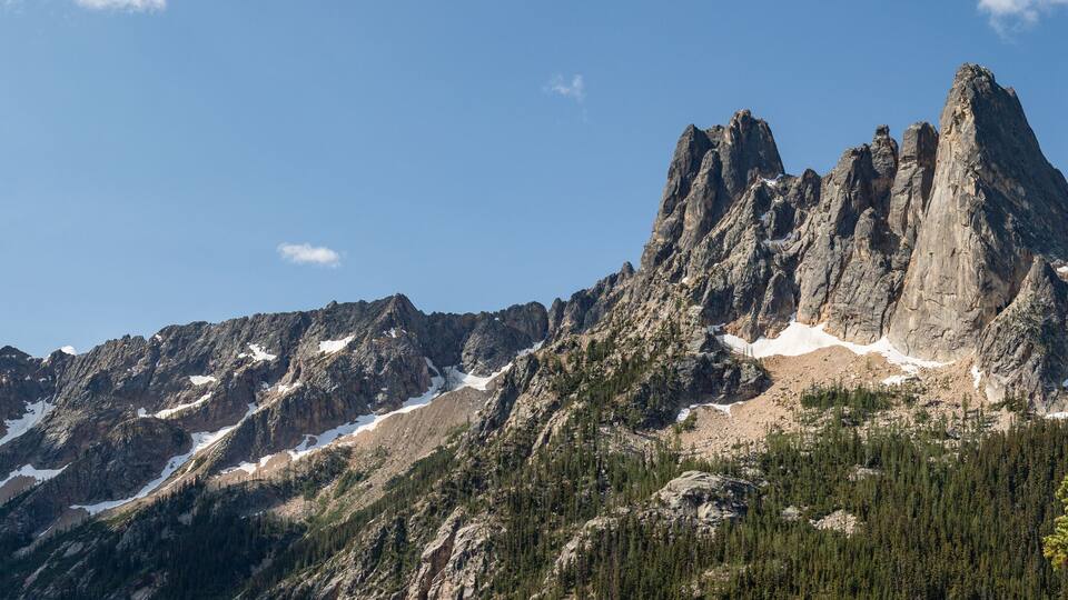 A rugged mountain range with prominent peaks and patches of snow.