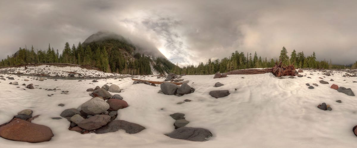 A snowy landscape with scattered rocks and a forested mountain in the background.