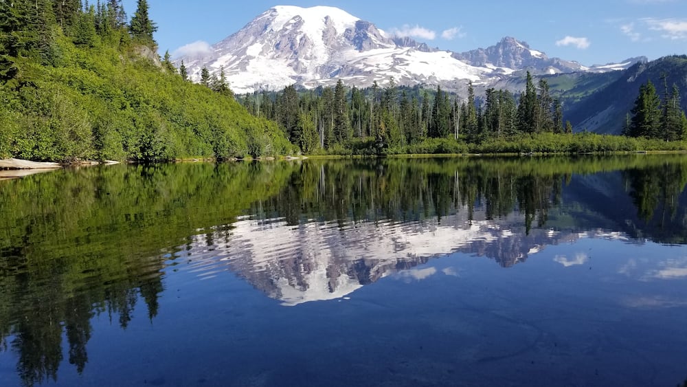 Ein ruhiger See, der einen mit Schnee bedeckten Berg und einen dichten Wald spiegelt.