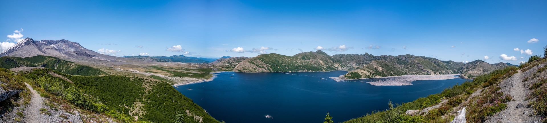 Paisagem montanhosa com um lago azul límpido, cercada por terreno acidentado e vegetação rala.