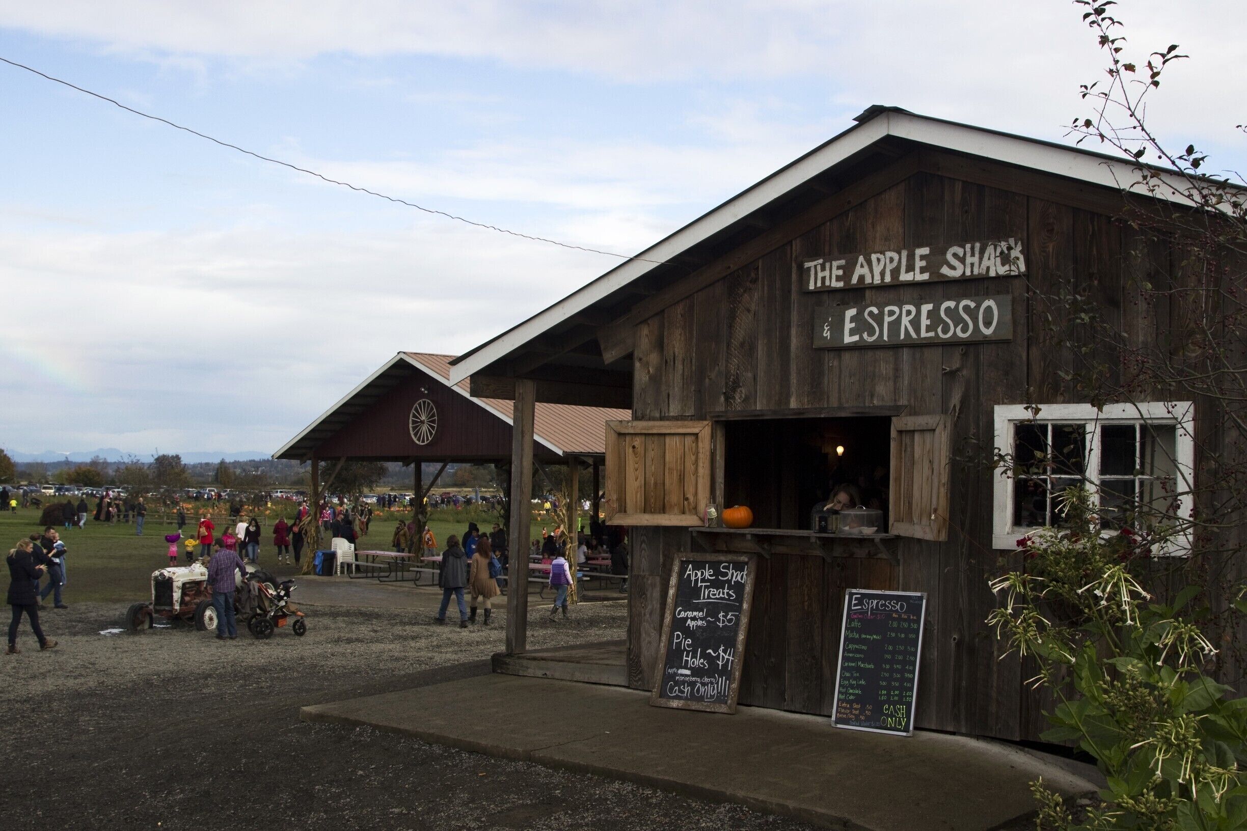 A rustic wooden building labeled "The Apple Shack Espresso" with a chalkboard menu listing apple treats and espresso.