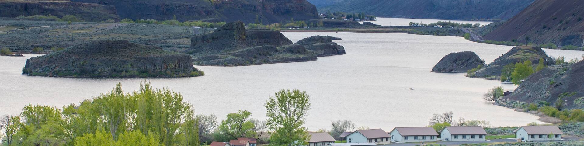 A river valley with cliffs, a small settlement, and a cloudy sky.