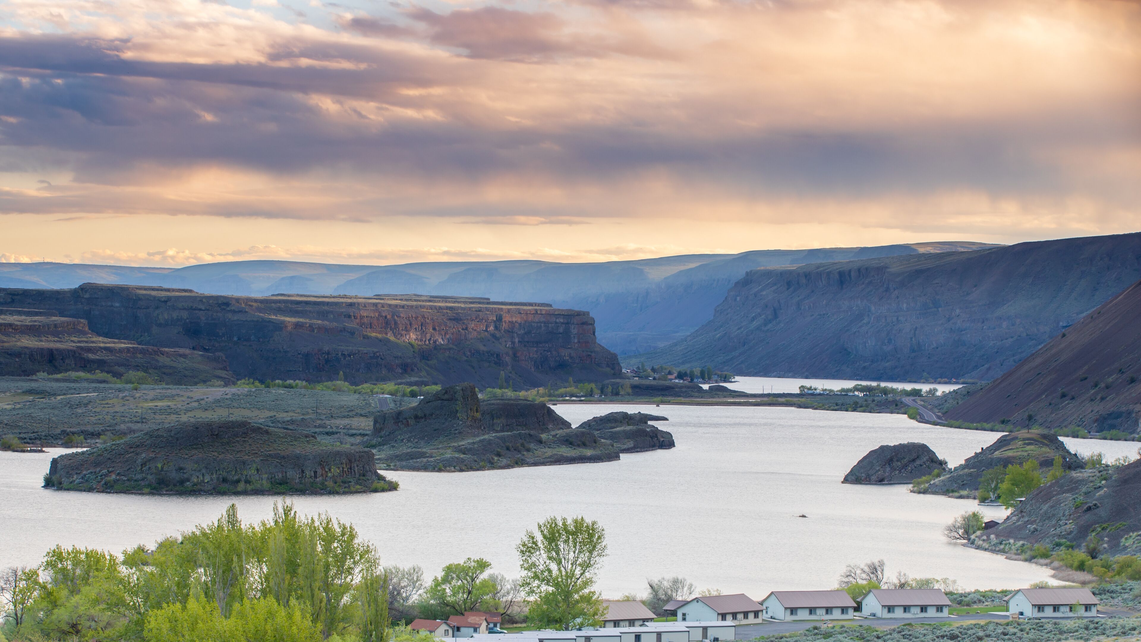 A river valley with cliffs, a small settlement, and a cloudy sky.
