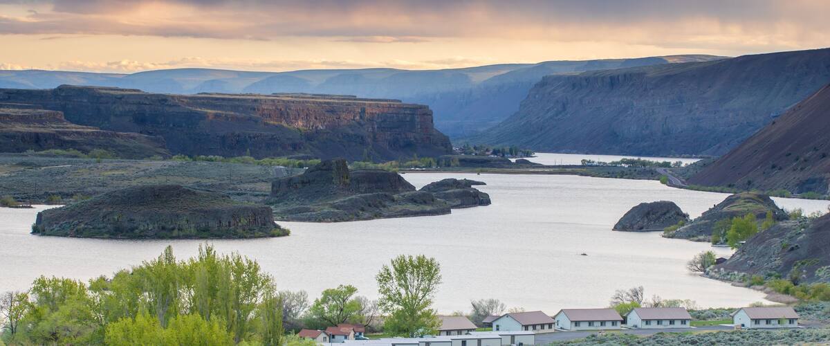 A river valley with cliffs, a small settlement, and a cloudy sky.
