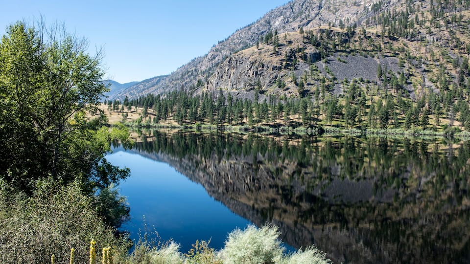 A calm lake reflecting trees and mountains.