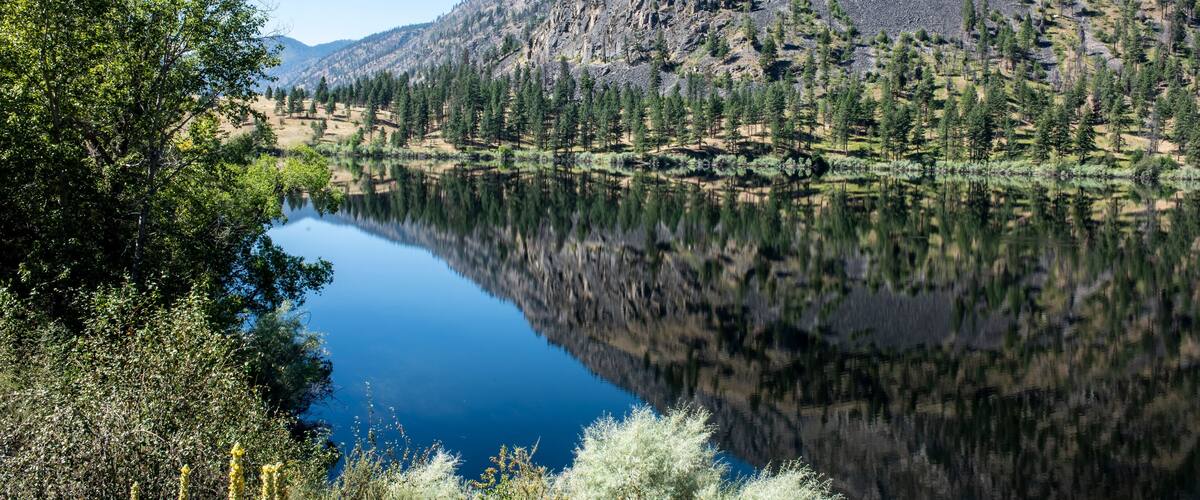 A calm lake reflecting trees and mountains.