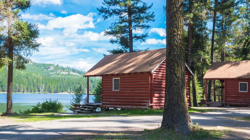 A red cabin by a lake surrounded by trees.