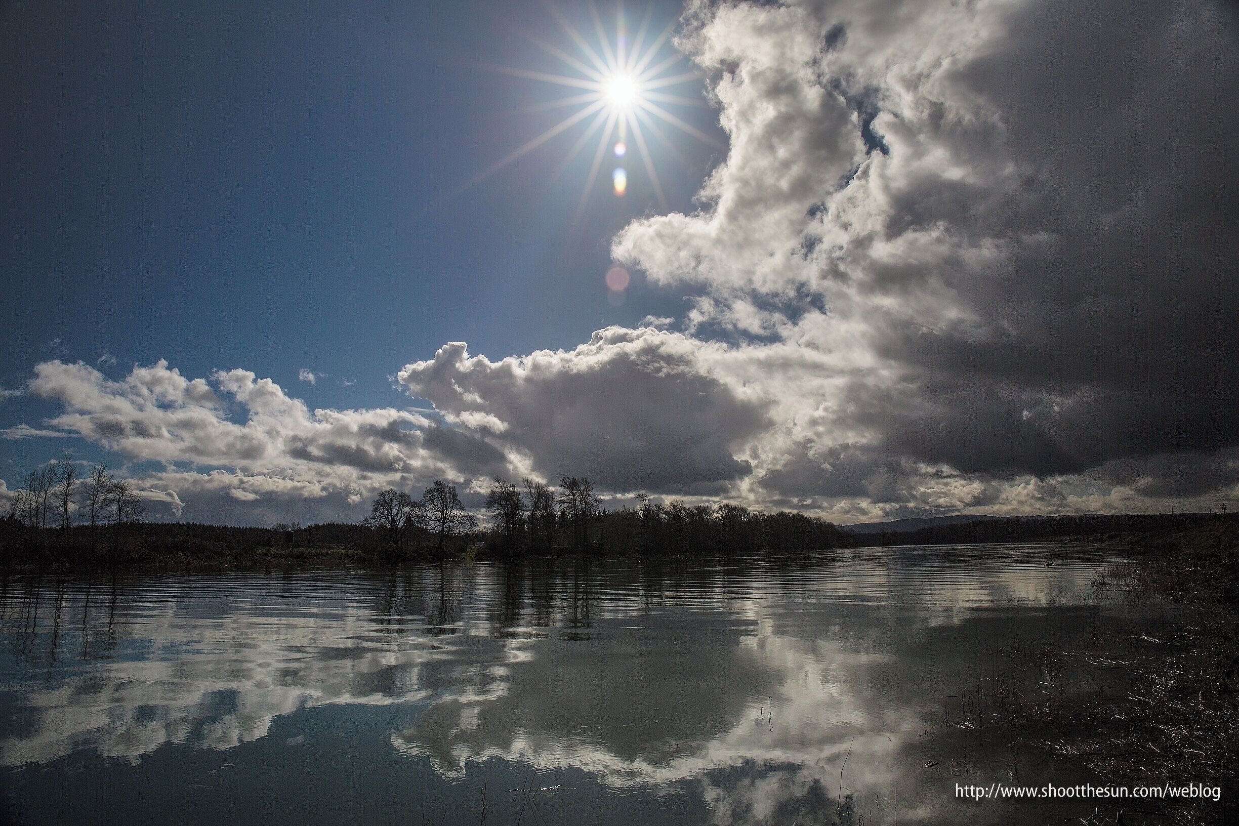 A lake with reflections of clouds and trees under a bright sun.