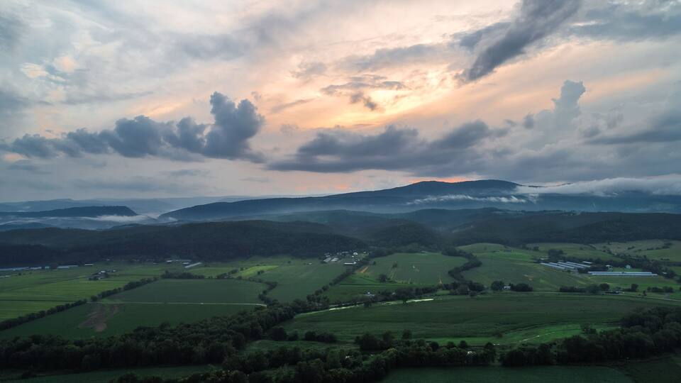 Rolling green hills, a valley, and a mountain range under a cloudy sky.