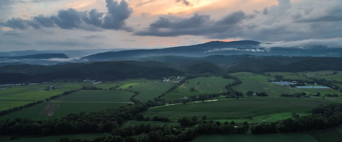 Rolling green hills, a valley, and a mountain range under a cloudy sky.