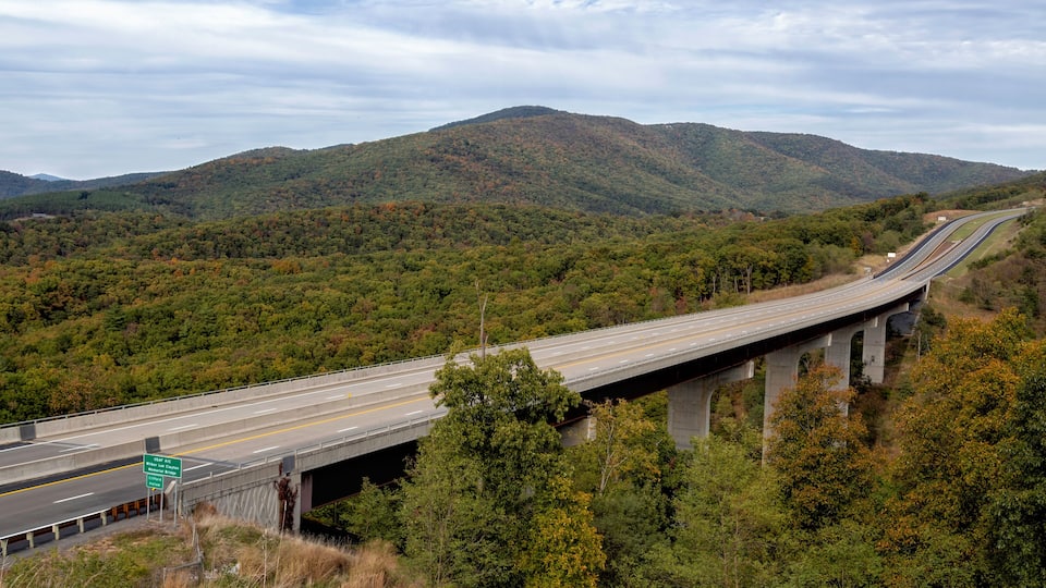 A highway bridge over a forested valley with mountains in the background.