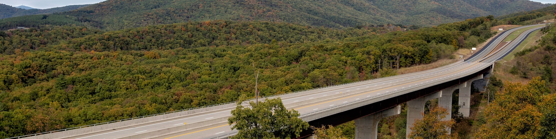 Un puente de autopista sobre un valle boscoso con montañas al fondo.