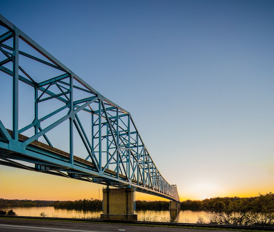A blue steel bridge over a calm river at sunset.