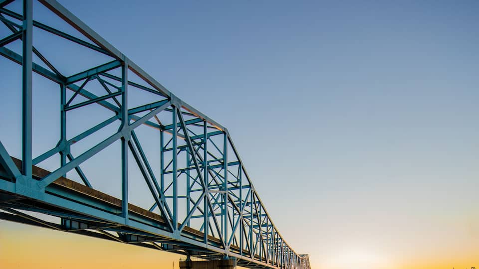 A blue steel bridge over a calm river at sunset.