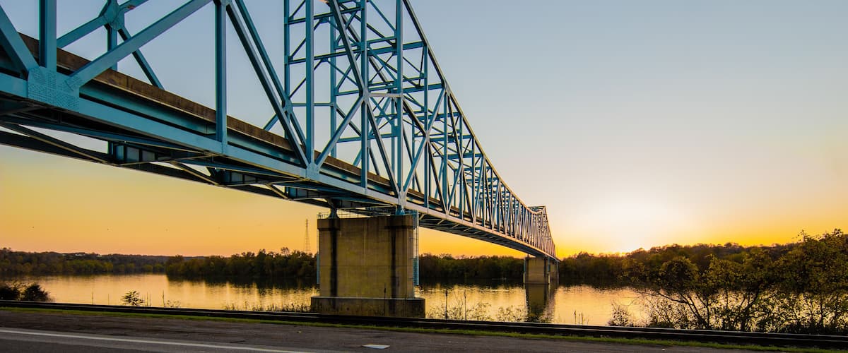 A blue steel bridge over a calm river at sunset.