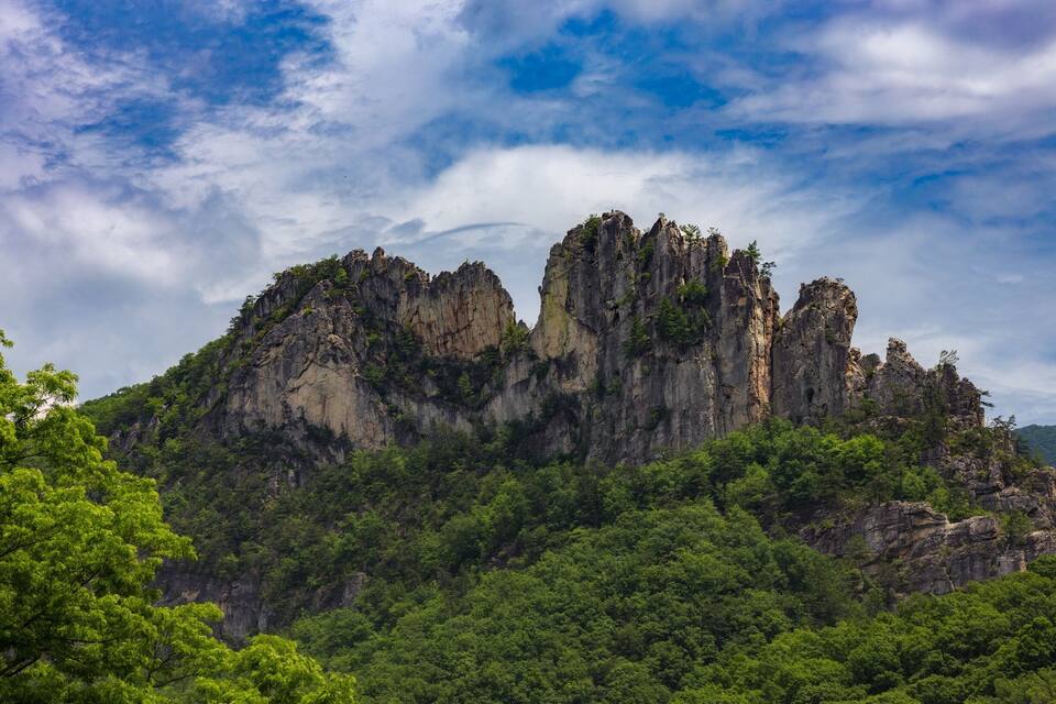Una montaña escarpada con formaciones rocosas destacadas y un denso bosque verde.