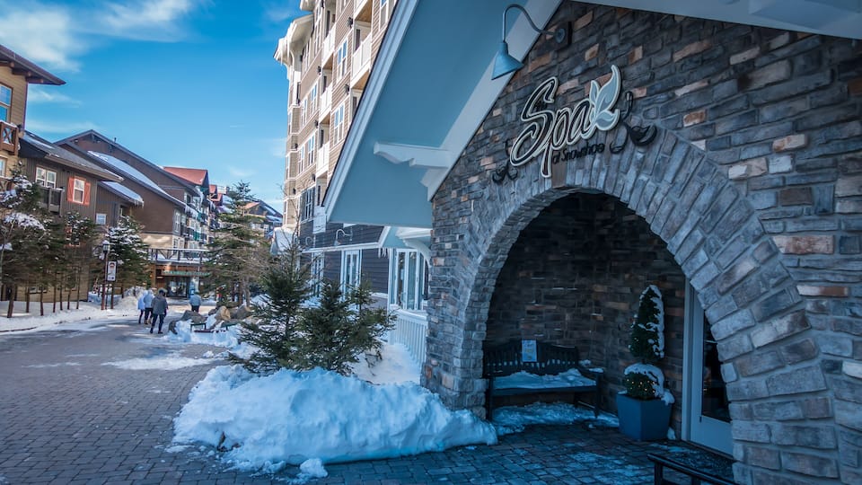 A snow-covered street with a stone archway leading to a building with a sign that reads 'Spa.'