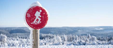 Red snowshoe hiking sign symbol with snovy trees and blue sky in winter snowscape landscape