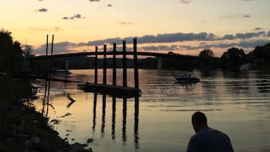 Um pôr do sol sobre um rio calmo, com uma ponte e barcos.