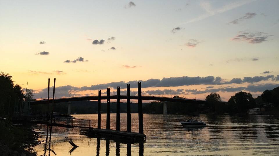 A sunset over a calm river with a bridge and boats.