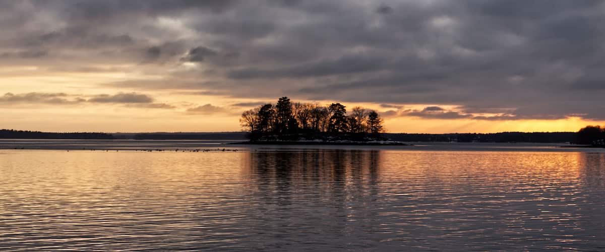 A calm lake at sunset with a small island of trees in the center.