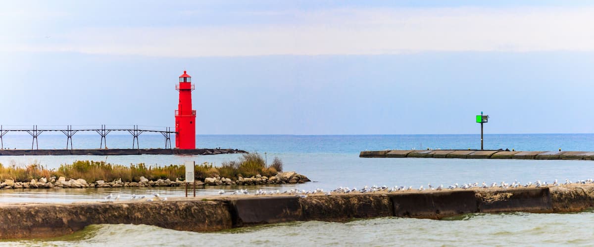 A red lighthouse, a green sign, and a pier extending into the water.