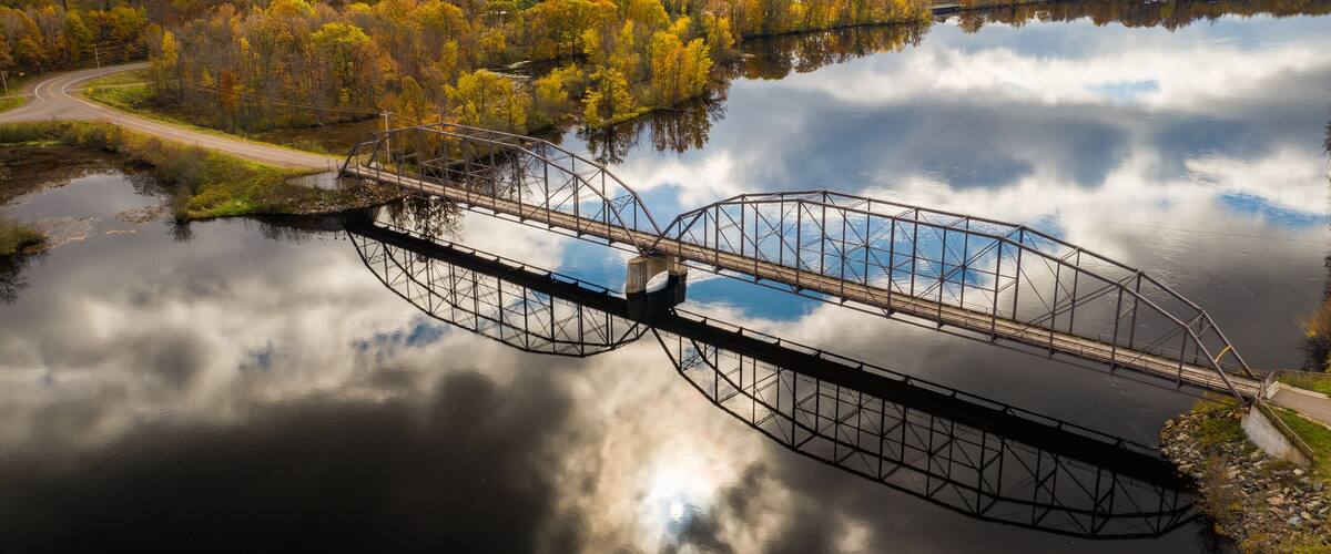A steel bridge over a calm river surrounded by autumn foliage.