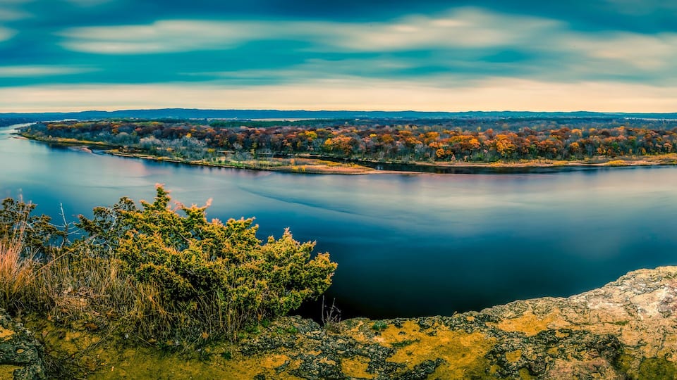 A calm lake surrounded by autumn-colored trees and rocky terrain.