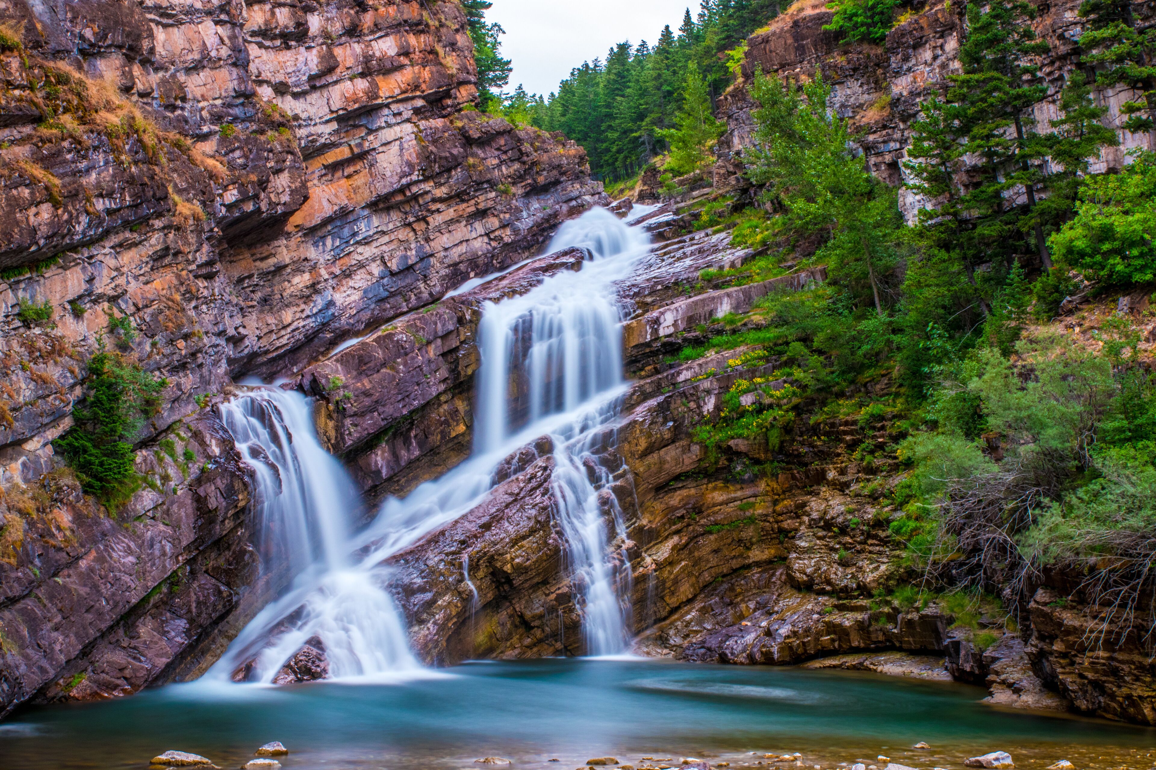A multi-tiered waterfall cascading down a rocky cliff surrounded by lush greenery.