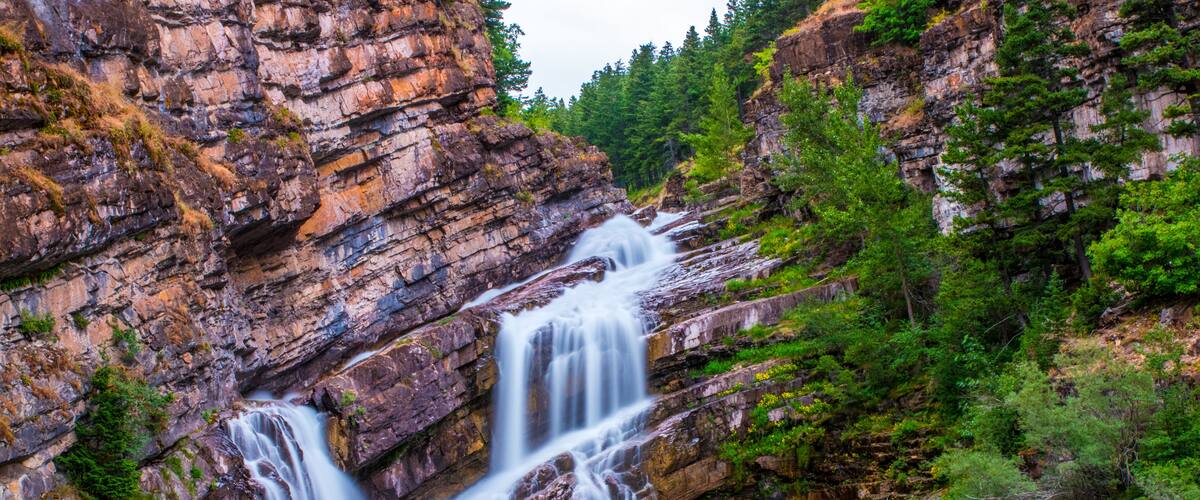 A multi-tiered waterfall cascading down a rocky cliff surrounded by lush greenery.