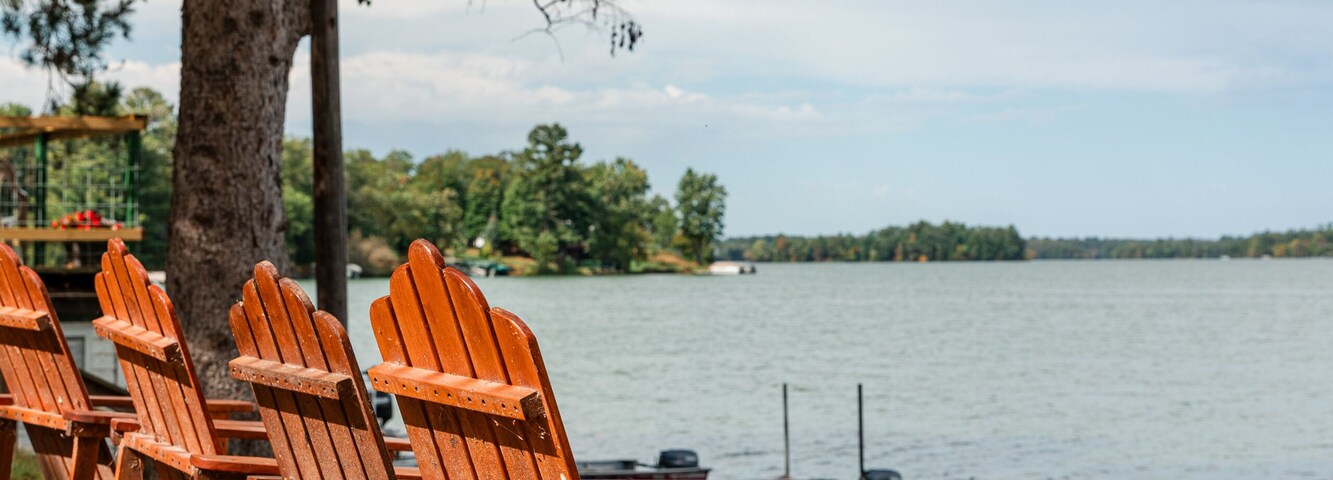 Sillas Adirondack de madera junto a un lago con un muelle y un bote.
