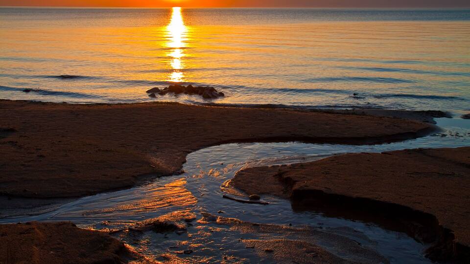 A sunset over a beach with a calm sea and a small stream.