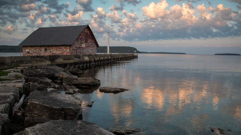 A rustic wooden building by a calm lake with a pier extending into the water, surrounded by large rocks.