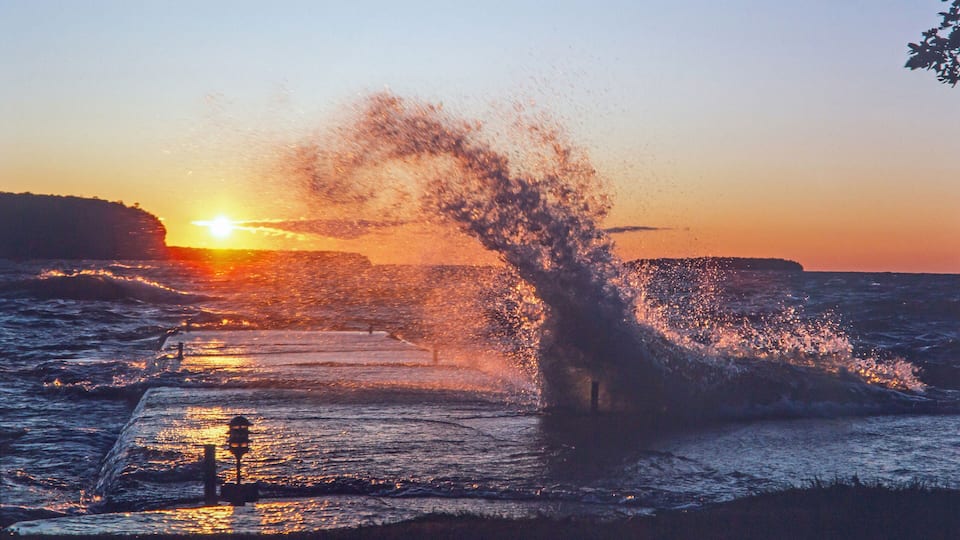 A sunset over a rocky coastline with waves crashing onto the shore.