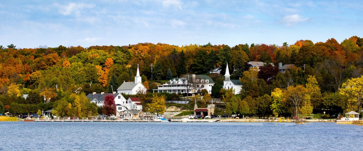 A lakeside town with autumn foliage, a church, and a white building with a green roof.